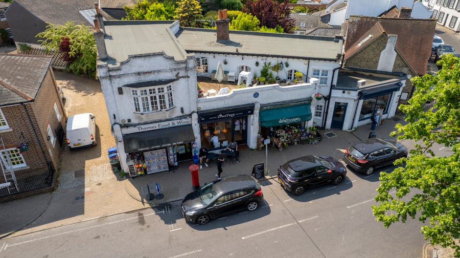 An aerial view of a small retail row on Guildford High Street, Surrey, featuring several shops including a florist with a green and black awning. In front of the shop, there are display racks with flo